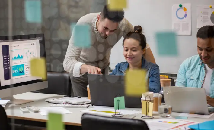 A group of professionals collaborates around a table with laptops, charts, and sticky notes, discussing data insights and strategies A group of professionals collaborates around a table with laptops, charts, and sticky notes, discussing data insights and strategies